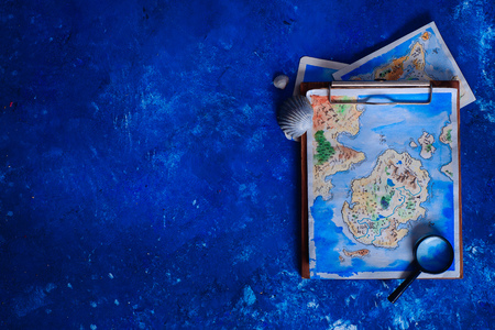 Sea travel and painting concept. Watercolor fantasy map on a wooden clipboard with a magnifying glass on a navy blue background with copy space.の写真素材