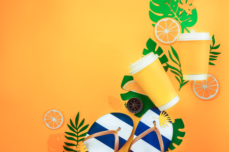 Summer vacation flat lay with tropical leaves, a refreshing drink and beach flip-flops on a sunny yellow background with copy spaceの写真素材