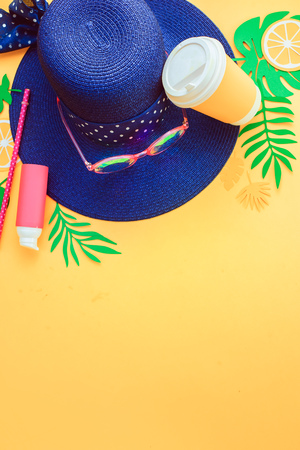Beach hat, sunglasses, lotion, refreshing drink and tropical leaves on a bright yellow background. Summer vacation concept with copy space.の写真素材