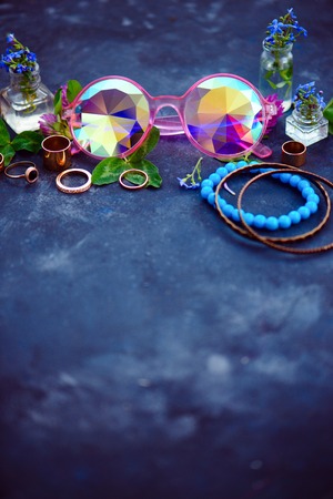 Stylish pink kaleidoscopic sunglasses with golden bracelets and rings in a feminine style concept with clover flowers on a dark background. Beautiful summer accessories.の写真素材