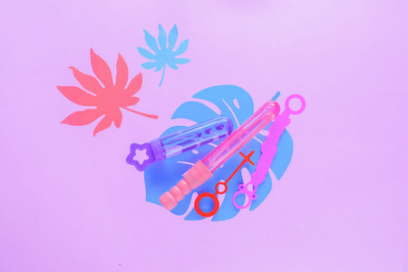 Bubble wands on a pastel purple background with tropical leaves and copy space. Summer flat lay...