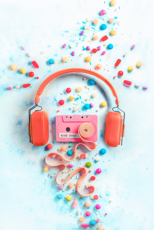 Headphones with a pink cassette tape with a tape of bubble gum in a gentle and sweet music concept with copy space. Candies, sprinkles, and marmalades in a pastel color flat lay with sweetsの写真素材