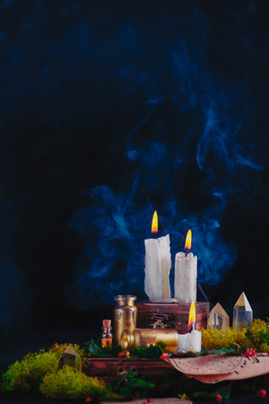 Burning candles in a witch or wizard workplace. Magical still life with crystals, potion bottles and moss. Occult equipment with copy space on a dark backgroundの写真素材