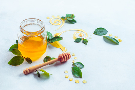 Honey in a small glass jar with a honey stick on a white background with copy space. Decorative honey swirls in high keyの写真素材