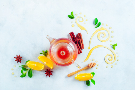 Honey and tea header. Glass teapot with decorative honey swirls, lemon slices and green leaves. Home remedies flat lay on a white background with copy spaceの写真素材