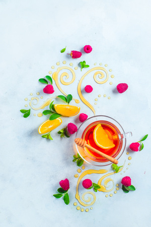 Honey tea from above. Decorative honey swirls, lemon slices, berries and tea in a glass cup on a white wooden background with copy space. Creative food flat layの写真素材