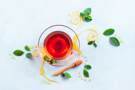 Glass cup of tea with decorative honey swirls and green leaves. Home remedies flat lay on a white background with copy spaceの写真素材