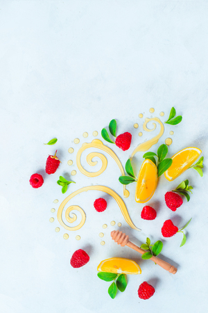 Honey dipper on white background with berries and lemon slices. Decorative honey swirls with green leaves. High key flat lay with copy spaceの写真素材