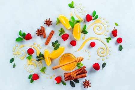 Honey dipper and honey in a jar on white background with berries, cinnamon and lemon slices. Decorative honey swirls. High key home remedies flat lay with copy spaceの写真素材