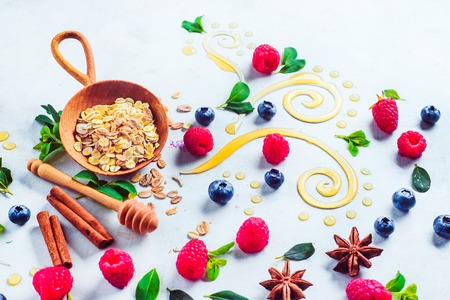 Oatmeal with honey, cinnamon, and berries. Raw ingredients with decorative honey swirls on a white wooden background with copy spaceの写真素材