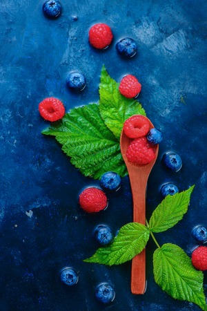 Summer berries in wooden spoons top view. Raspberry and blueberry mix on a dark blue wet background with copy space. Raw ingredients from aboveの写真素材
