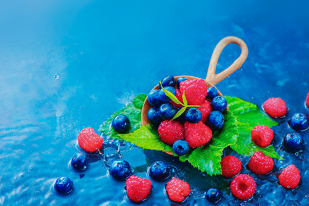 Summer berries in a round wooden spoon with raindrops. Raspberry and blueberry mix on a dark blue wet background with copy space. Raw ingredients conceptの写真素材
