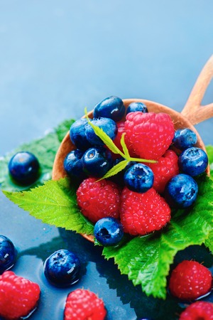 Summer berries in a round wooden spoon with raindrops. Raspberry and blueberry mix on a dark blue wet background with copy space. Raw ingredients conceptの写真素材