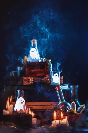 Little ghosts in glass jars. Halloween concept on a dark background with a stack of magical books and mysterious smoke.の写真素材