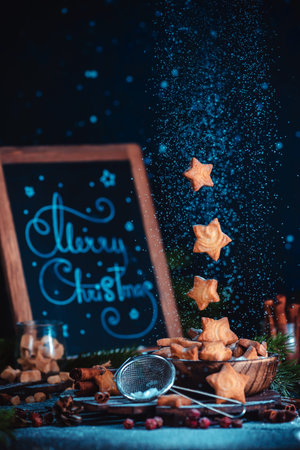 Flying star-shaped cookies with sugar powder and Merry Christmas lettering. Traditional baking concept on a dark background with copy spaceの写真素材
