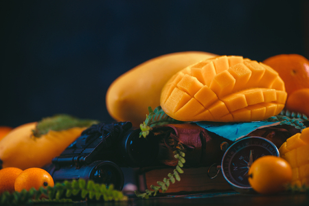 Cut mango halves close-up header with oranges, kumquat, and other tropical fruits. Dark background with copy space. Discovery of exotic fruits concept.の写真素材