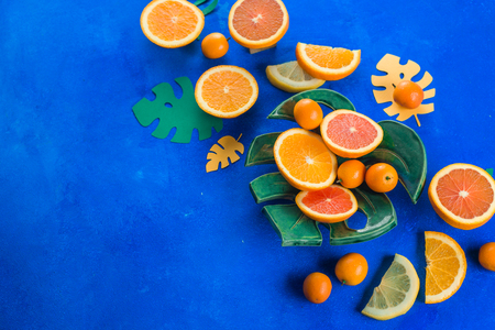 Mango, oranges, kumquat and other tropical fruits on a monstera plate. Bright blue background with copy space. Exotic food header.の写真素材