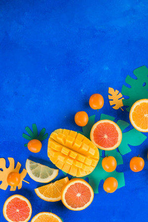 Tropic fruits on a vibrant blue background with copy space. Mango, oranges, kumquat, and other exotic fruits.の写真素材