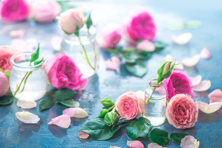 Glass bottles with pink peony roses on a light background with copy space. Feminine header with petals and flowers in pastel tonesの写真素材