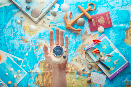 Hand holding a compass above map with wooden anchor, paper airplanes, passport and a magnifying glass. Adventure flat lay with copy spaceの写真素材