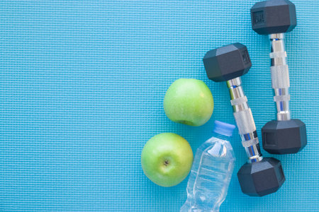 Empty space for the text. Slimming. Two green apples, bottle of water and dumbbells lie on the...