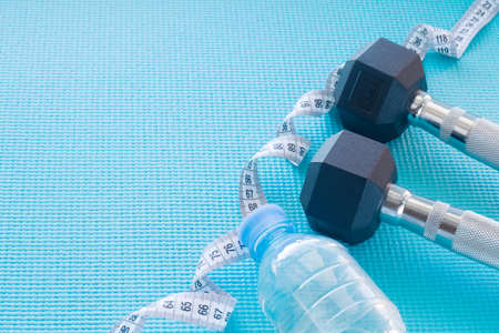 Empty space for the text. A measuring tape, dumbbells, a bottle of water on a sports matの写真素材