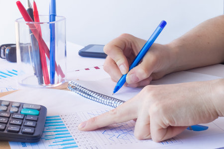 Workplace in the office. Hands with a pen. Paper, graphics, pens, pencils. Blue, red, white.