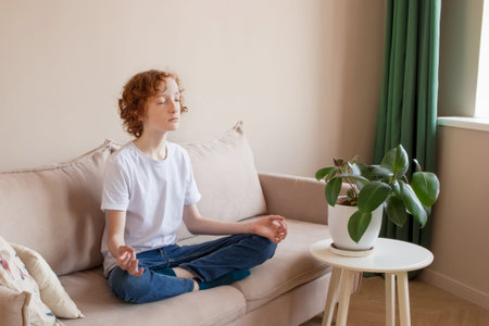 Empty space for text. A teenage boy 14-16 sits on the couch at home and meditates.の写真素材