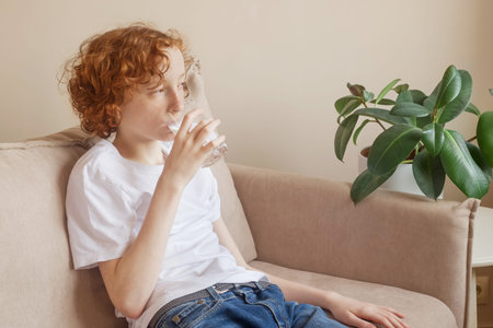Empty space for text. Teenager drinks water from a glass indoors.