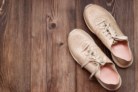 Empty space for text. A pair of women's summer sports shoes in gold color on a brown wooden backgroundの写真素材