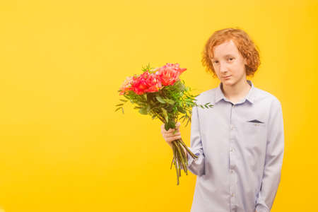 An empty space for the text. A boy stands with a bouquet of flowers on a yellow background.の写真素材