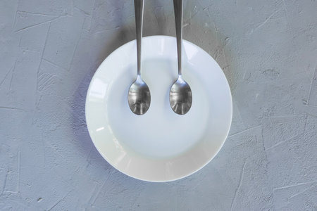 An empty white plate and two spoons on a gray background.の写真素材