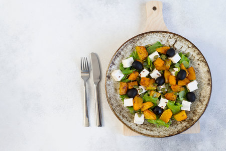 Healthy salad with fried pumpkin, feta cheese, olives, salad greens, pumpkin seeds on the light gray background. Horizontal view. Top view. Free spaceの写真素材