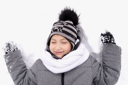the boy is lying in the snow and smiling. He is outdoor. It is winter.