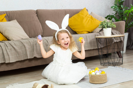 litlle girl is smiling and playing with easter eggs in light room at home.