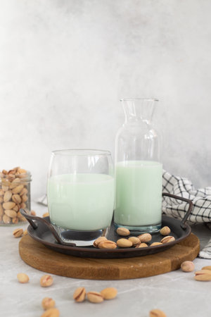 pistachio milk in a glass and in a bottle with pistachios on a plate grey background. vertical frame.の写真素材