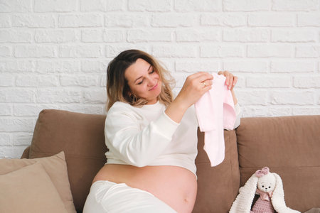 Beautiful pregnant woman is holding cloth of baby.の写真素材