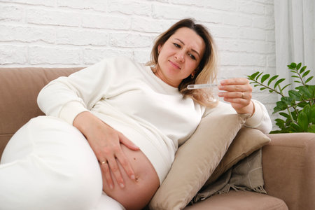 Pregnant woman lying on the couch and looking at the thermometer