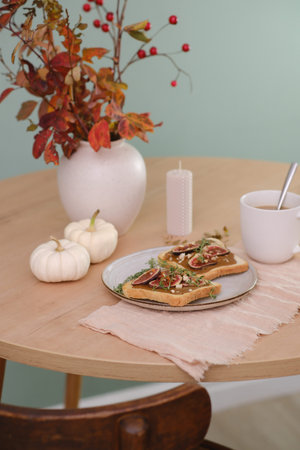 Home autumn breakfast, two toasts with almond butter, figs, coffee, pumpkins, candle, ceramic vase with red leaves on a round wooden tableの写真素材