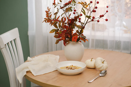 Breakfast table - oatmeal porridge with pumpkin and nuts, vase with autumn branches, pumpkins, linen...