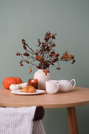 Autumn home breakfast- plate with croissant, ceramic vase with dry berries branches and yellow...