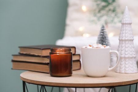 Christmas home decorations - burning candle, books, cup of cocao with marshmellow, ceramic christmas...