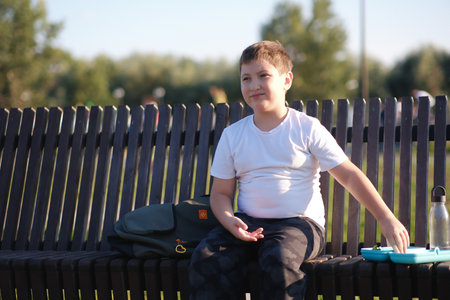 a cute boy of eight years with headphones sit on bench and have break outdoor.の写真素材