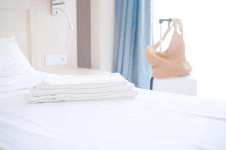 Clean towels on bed at hotel room. Bed maid-up with clean white pillows and bed sheets in beauty bedroom with white suitcase on background. Close-up. interior background.の写真素材