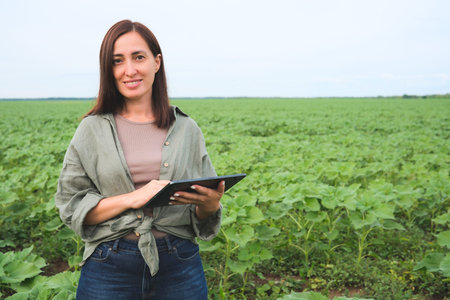Agronomist woman inspecting sunflowers growing in the farm field in summer. Agriculture production...