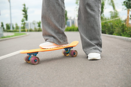Cropped shot of woman legs in sneakers standing on skateboard while riding outdoor. Sport and urban...