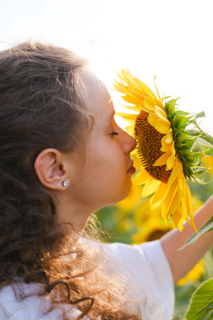 A Young Girl Joyfully Embracing a Tall Sunflower in a Beautifully Bright Flower Fieldの写真素材