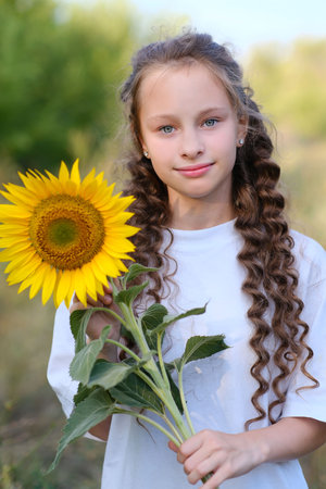 A joyful girl holding a vibrant sunflower, surrounded by beautiful nature and greeneryの写真素材