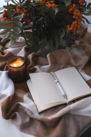 A Cozy Autumn Setting Featuring a Journal, Flickering Candle, and Beautiful Flowersの写真素材