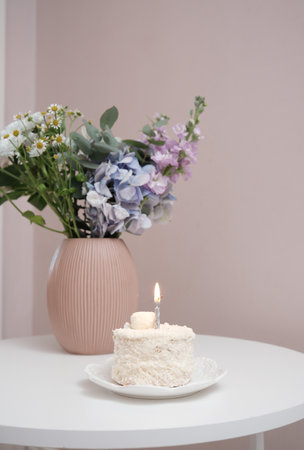 An Elegant Cake embellished with a Candle and Beautiful Flowers displayed on a Tableの写真素材
